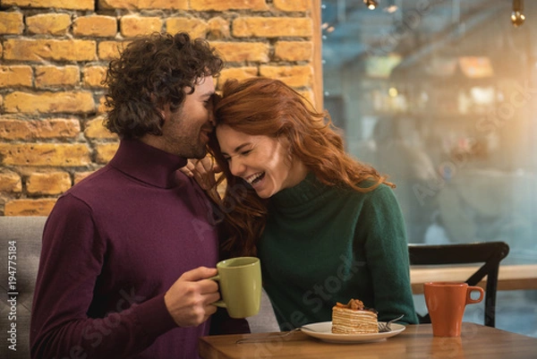 Obraz Joyful loving couple is entertaining in cafe together. They are drinking tea with cake and laughing