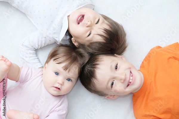 Obraz happy kids, three laughing children different ages lying, portrait of boy, little girl and baby girl, happiness in childhood of siblings, living in big family with three children