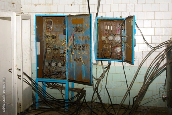 Obraz Old dismantled and rusty electrical panel assembly on an abandoned and destroyed factory against a backdrop of chaos. Destruction and vandalism. Ukraine.