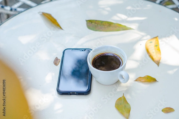Fototapeta Close up smart phone and white coffee cup on the white table with white white background