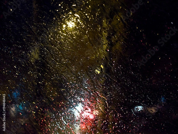 Fototapeta Raindrops on the car window at night illuminated by street lights
