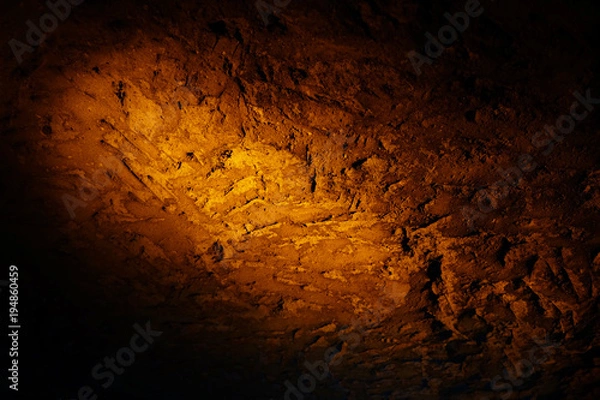Fototapeta Natural texture created on the wall in the underground cave in Mazi underground city, Sehri, Turkey, enlightened by orange color spotlight