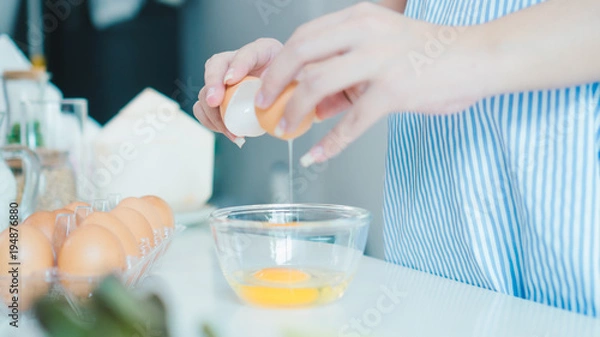 Fototapeta Woman cracking an egg into a bowl with  standing by in kitchen. Mother pregnant cooking in kitchen.