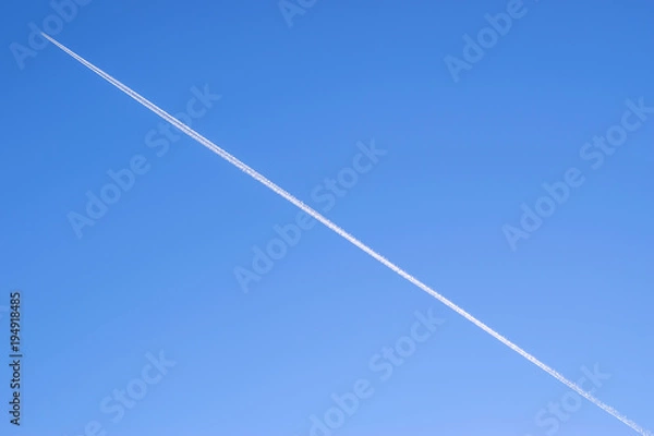 Fototapeta blue background of the sky with a flying plane on it with a white Condensation trail contrail behind it on the entire sky diagonally