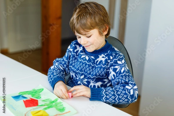 Fototapeta Little kid boy making paper origami tulip flowers for a postcard for mother's day or birthday. Cute child of elementary class school doing handicraft
