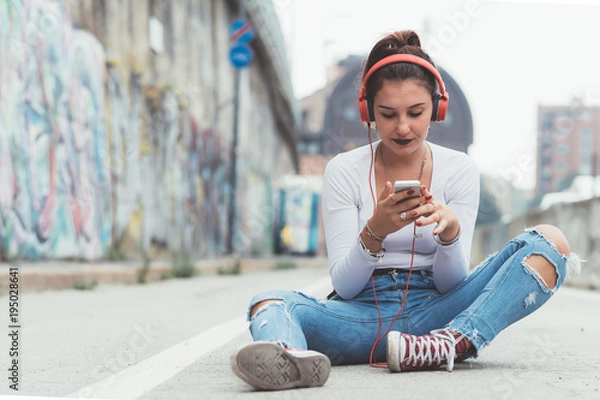 Fototapeta young woman outdoors listening music with headphones using smart phone - relaxing, enjoying, technology concept