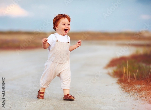 Obraz adorable redhead toddler baby boy in jumpsuit running through the summer road and field
