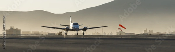 Fototapeta Beautiful morning sunrise over the apron of Uyuni airport, best of aviation photography; with a colorful red windsock and Uyuni village on the background