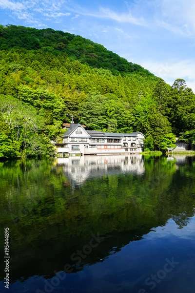 Fototapeta Beautiful abundant natural shades of spring green mountain background mirror reflection on fresh lake Kinrinko with buildings and blue sky, Yufuin