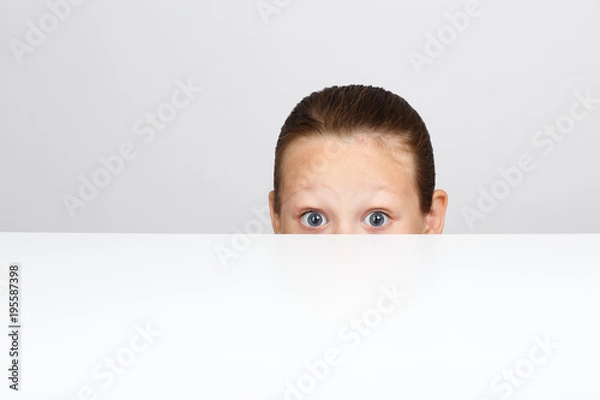 Fototapeta Pod stołem chowa się mała dziewczynka ze strachem w oczach.