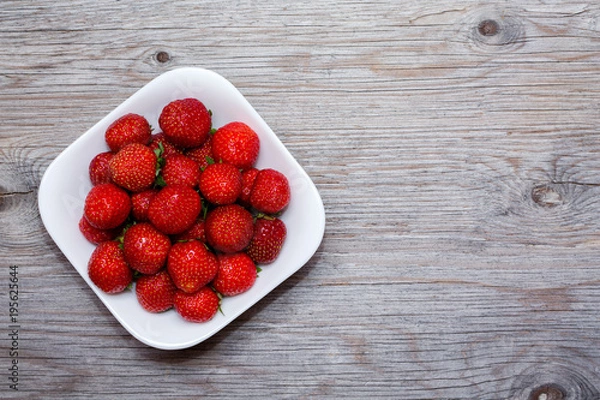 Obraz Strawberries berries on a white plate on a wooden table. Copy text. Close up.