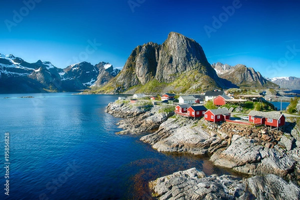 Fototapeta The village of Reine under a sunny, blue sky, with the typical red rorbu houses.