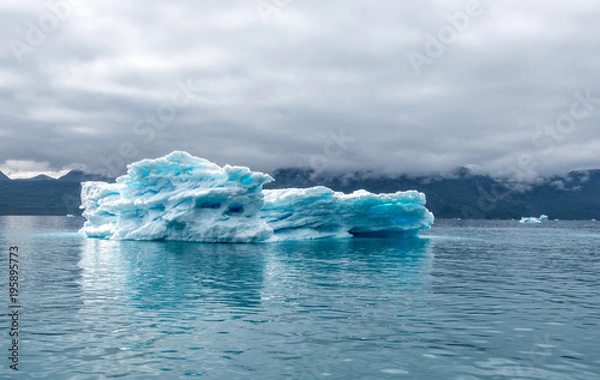 Fototapeta Greenland, Iceberg at a Fjord blue iceberg with with clear blue colour spots inside of it and also with dramatic mood of the sky in the atlantic ocean