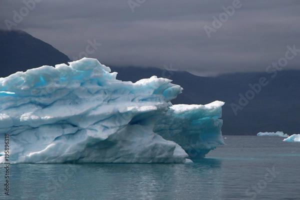 Fototapeta blue iceberg with lightblue spots inside of it and also with dramatic mood of the sky in the atlantic ocean