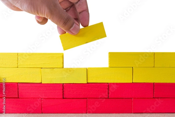 Obraz Concept of building success foundation, Hand on the last yellow puzzle wooden blocks in the shape of a wall isolated white background.