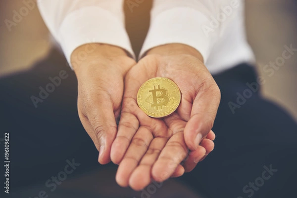 Fototapeta Hand of a businessman holding a bitcoin.The concept of money and exchange in cyberspace.