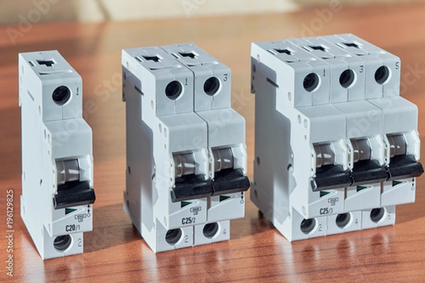 Obraz Three modular electrical circuit breakers on the table. The switch is single-pole, double-pole and three-pole. Protection of electrical wiring of household or home use. Distribution of electricity.