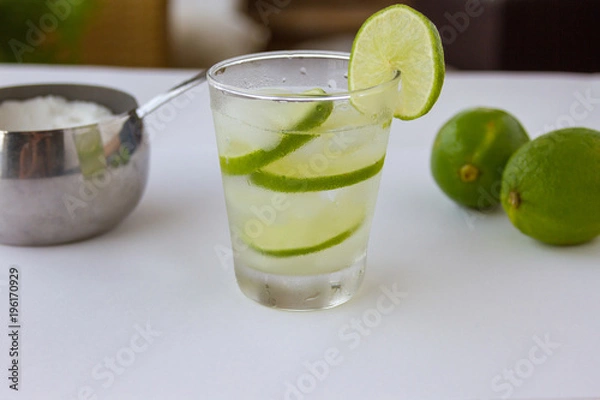 Fototapeta Summer drink -  Brazilian caipirinha, sugar bowl, limes . White background. Selective focus