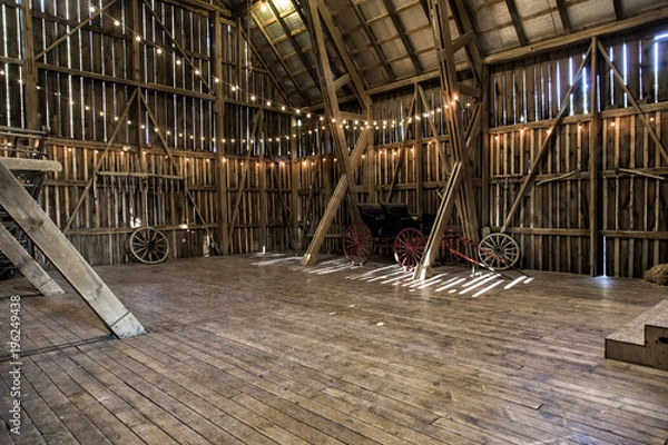 Fototapeta The interior of a barn with strings of lights and a buggy