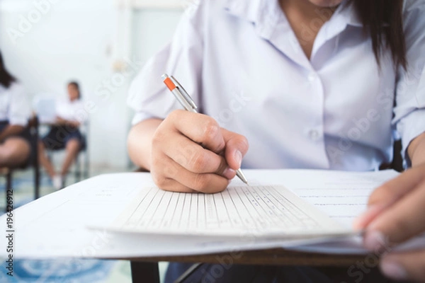 Fototapeta Students writing pen in hand doing exams answer sheets exercises in classroom with stress.