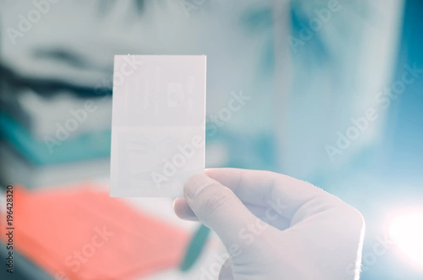 Fototapeta Close up on hand of a businessman holding white business card over blurry car office background. Professional person showing introduction