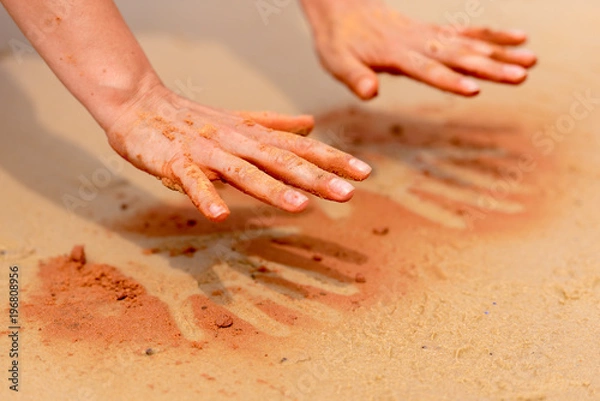 Obraz Woman hands creating shapes with red sand on the beach in aboriginal art style