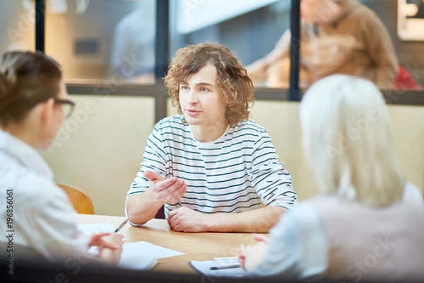 Fototapeta Young confident man explaining what he waiting of new job to employers during interview