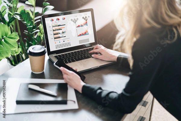 Obraz Rear view. Young businesswoman is working on laptop with graphs, charts, diagrams, schedules on screen. Online marketing
