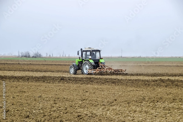 Fototapeta Lush and loosen the soil on the field before sowing. The tractor plows a field with a plow