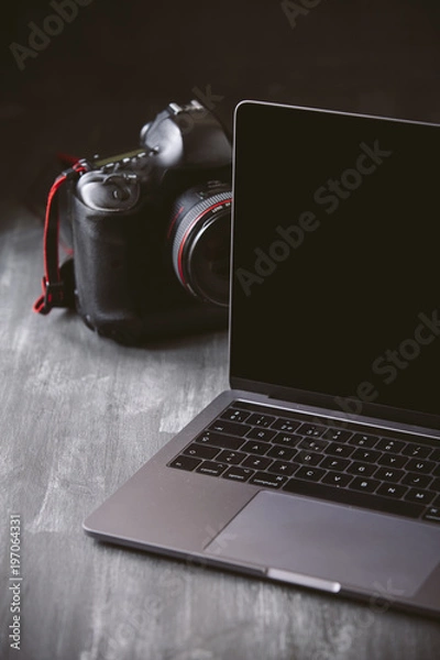 Fototapeta Laptop and a camera on a dark wooden background.