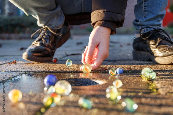 Fototapeta Child playing with marbles on yhe sidewalk. old-fashioned toys still in use today.