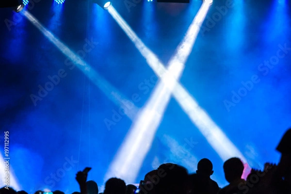 Obraz Concert crowd attending a concert, people silhouettes are visible, backlit by stage lights. Raised hands and smart phones are visible here and there.