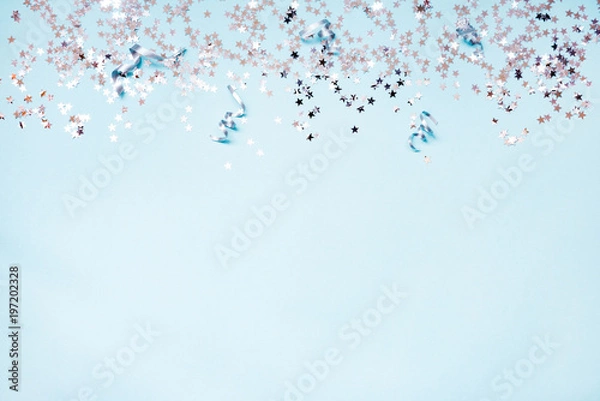 Fototapeta Star shaped silver sequins and silver ribbons over blue background. Copy space.