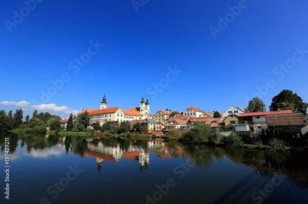 Fototapeta A fairy tale castle and old town with beautiful mirror reflections on smooth lake water under clear blue sky in Telc, a UNESCO world heritage site in Czech Republic, Europe 