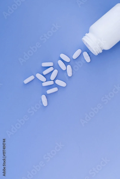 Fototapeta Pills are poured from a white bottle on a pastel blue background. Place for text.Flat lay