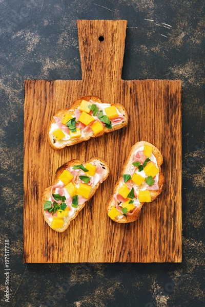 Fototapeta Toast with ham and mango on wooden Board, dark background, top view.