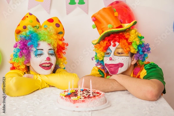 Fototapeta Clowns are a boy and a girl in bright costumes at the child's birthday. A table with refreshments and a cake. The explosion of emotions and the fun of the circus. greed and desire to eat cake