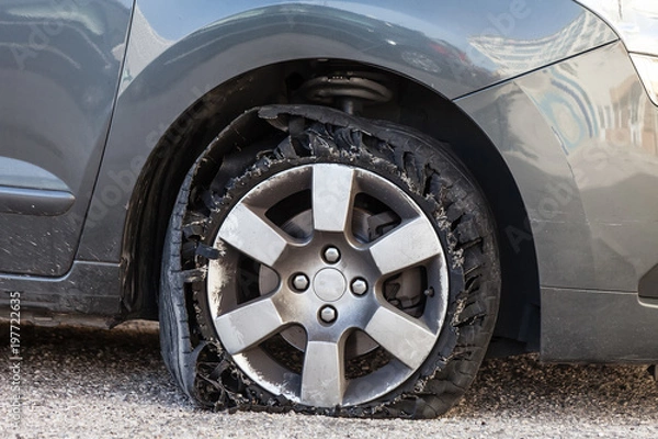 Fototapeta Destroyed blown out tire with exploded, shredded and damaged rubber on a modern suv automobile. Flat low profile tyre on an alloy rim, ripped open in pieces with visible interior.