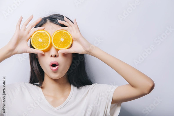 Obraz Studio portrait of young surprised funny girl holding two orange slices in t-shirt on white background and smiling. Fresh fruits and healthy diet concept. Free copy space provided