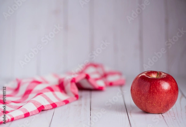 Fototapeta A single apple on a whitewashed wood top with a vintage red check dish towel.