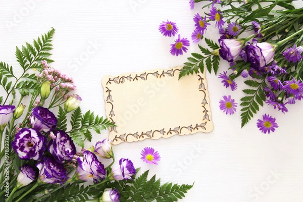 Fototapeta Top view of purple beautiful flowers arrangement and wooden board over white background. Copy space.