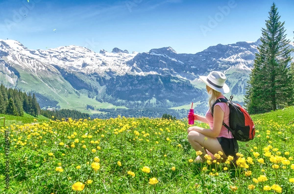 Fototapeta Alpy Szwajcarskie. Dziewczyna siedząca na trawie, pijąc wodę z butelki i podziwiając górską scenerię. Engelberg Resort