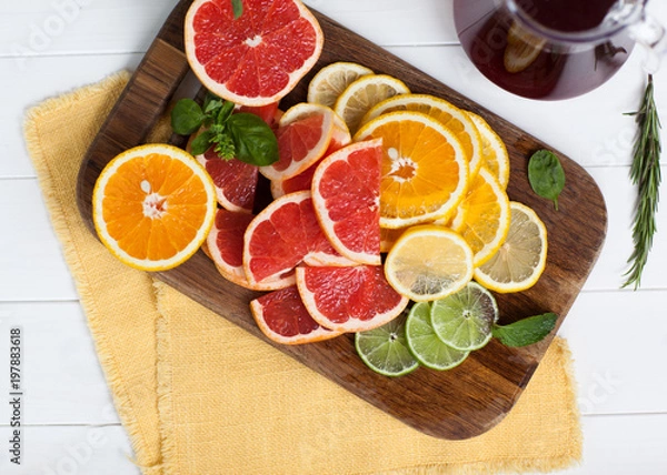Fototapeta sliced citrus decorated with basil on wooden and white backgrounds with orange towel. Orange, grapefruit, lime, lemon. Flat lay, top view.