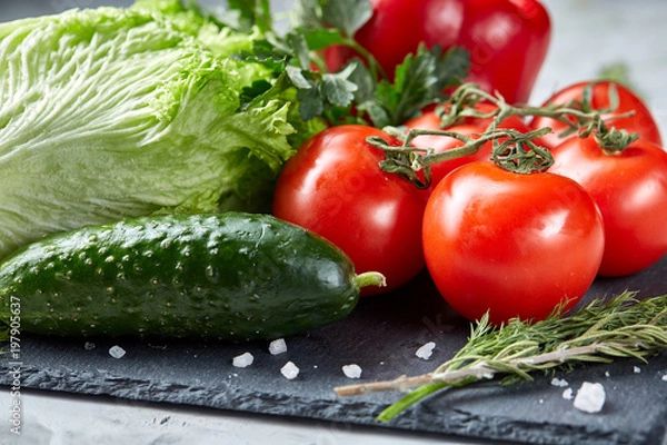 Fototapeta Bunch of fresh tomatoes with green leaves on stony board over white background, top view, close-up, selective focus