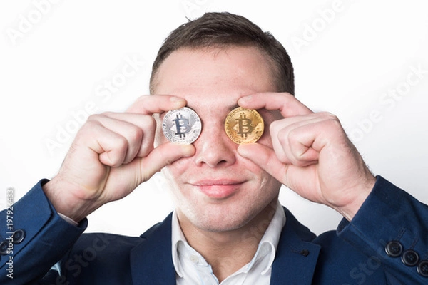 Fototapeta A man holds a coin bitcoin in front of his eyes. In the eyes of money (bitcoin)