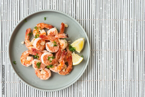Fototapeta Top view of cooked delicate shrimps with pieces of lemon and cut fresh greens on grey platter. Well-served, full of vitamins and diet dish. Copy space in right side