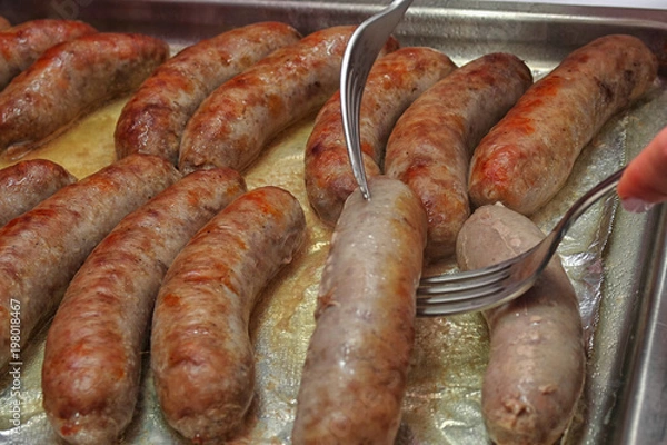 Fototapeta The process of frying home sausages on a tray, turning over with