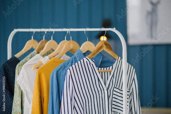 Fototapeta Clothes hang on wooden coat hangers in clothing store with home tone. Shopping and spending concept