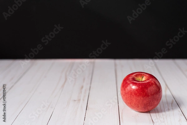 Fototapeta One red apple on a whitewashed wood countertop with a black background