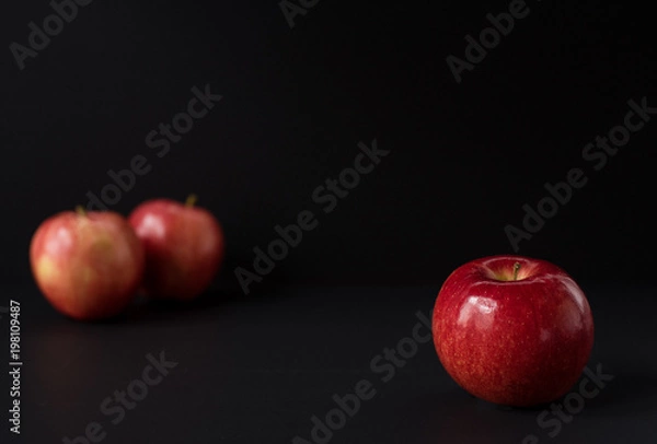 Fototapeta A shiny red apple isolated on black background. Two other apples out of focus in background